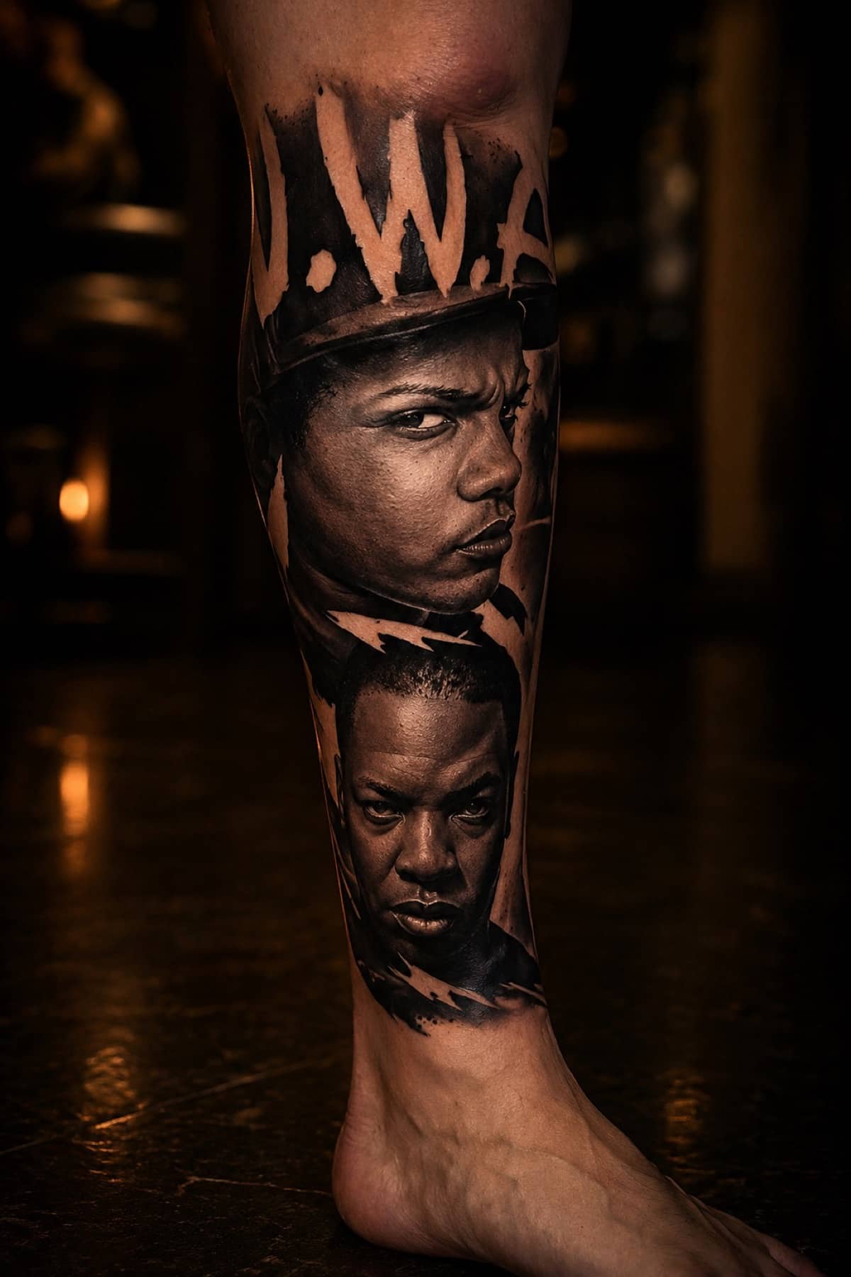 Black and grey N.W.A portrait leg tattoo with Eazy-E and Dr. Dre in realism at Bloodline Tattoo Bangkok